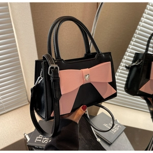 Close-up of black leather bag featuring a large pink bow and heart crystal detail