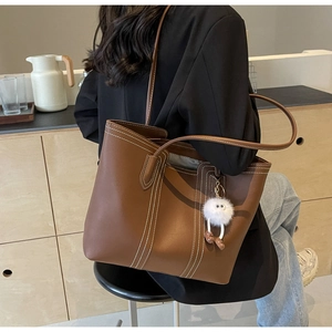 Close-up of brown leather tote bag with white contrast stitching and plush ball charm