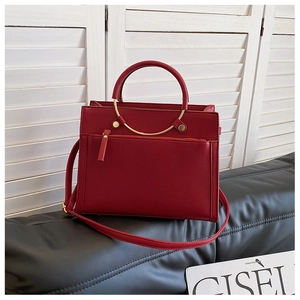 Detail of red litchi texture leather handbag with metal handle on a black cushion