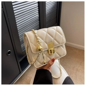 Detail of white quilted crossbody bag with gold chain strap and metal bead decoration