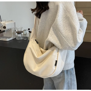 Detail of cream canvas crescent bag with black zipper and woven label on shoulder strap