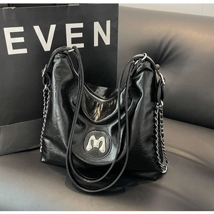 Detail of black wrinkled PU leather hobo bag with metallic M logo and silver chain straps