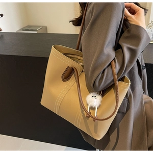 Detail of light brown tote bag featuring white contrast stitching and plush eye charm