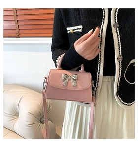 Detail of pink crossbody bag with silver bow accent shown on a model for size reference