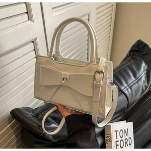 Close-up of white leather handbag featuring a large bow and sparkling heart rhinestone