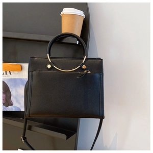 Detail of black pebbled leather crossbody bag with golden ring handle on a display stand