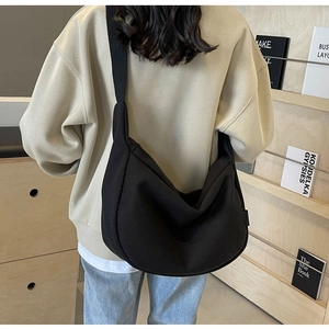 Detail of a black canvas half-moon crossbody bag shown on a shoulder in a cozy library