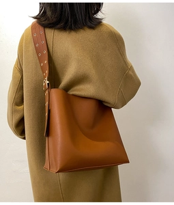 Détail du sac seau en cuir marron avec large bandoulière et œillets métalliques