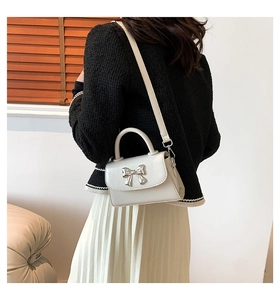 Detailed view of cream white crossbody bag with silver bow clasp worn by a model
