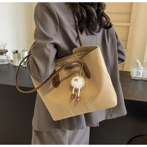 Detail of khaki tote bag with contrast brown trim and plush charm worn by a model