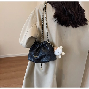 Detail of black pebbled leather bucket bag with gold chain strap and plush sheep charm