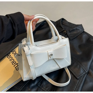 Close-up of white leather handbag with bow detail and heart-shaped rhinestone center