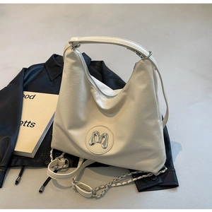 Detail of cream hobo bag with metal M logo and mixed chain strap on leather jacket