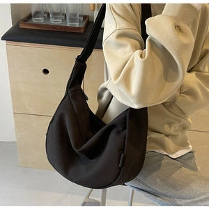 Detail of a black canvas crescent crossbody bag worn by a model in a warm indoor setting