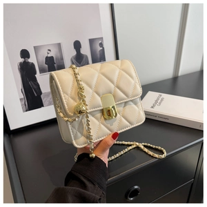 Detail of cream quilted crossbody bag featuring gold chain strap and metal ball buckle