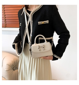 Detail of cream white mini crossbody bag with a silver bow and sleek round handle