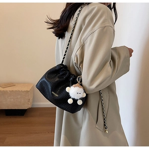 Detail of black crocodile embossed bucket bag with gold chain and plush sheep charm
