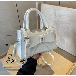 Close-up of white crossbody bag with bow decoration and heart rhinestone on leather