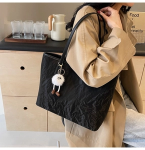 Detail of black pleated tote bag with a cute plush charm on a model in trench coat
