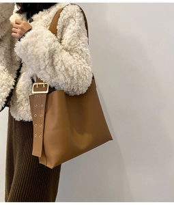 Détail de la large bandoulière réglable avec boucle dorée sur un sac seau marron