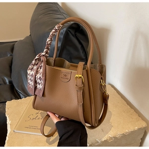 Close-up of brown textured leather bucket bag with silk scarf handle and logo detail