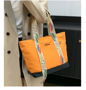 Détail du sac cabas en toile orange avec bandoulière fleurie et logo brodé