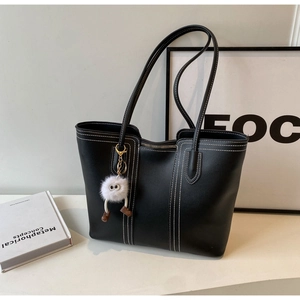 Detail of black leather tote bag with white contrast stitching and plush charm decoration