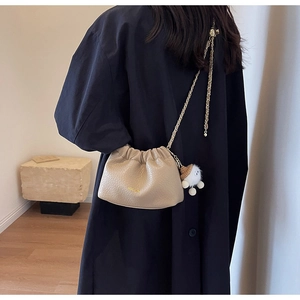 Detail of beige pleated cloud bag with gold chain and plush cloud charm worn by model