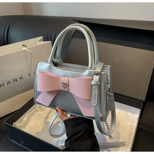 Detail of silver handbag featuring a pink bow with heart rhinestone and thin strap