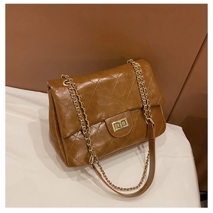 Detail of brown quilted leather texture and gold chain strap on small square bag