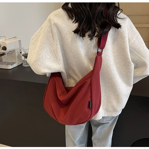 Dark red canvas crossbody moon bag shown in a stylish back view on a female model