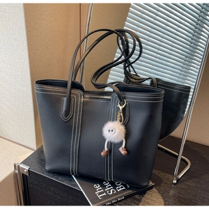 Detail of black tote bag with white stitching and fuzzy monster charm on wood table