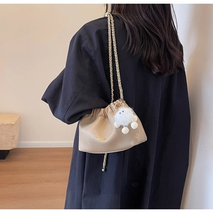 Detail of beige pleated cloud bag featuring gold chain strap and plush doll pendant