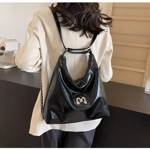 Close-up of black glossy oversized tote bag featuring silver metal M logo detail