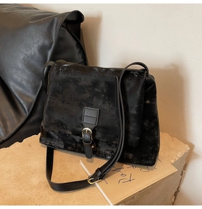 Detail shot of black vintage tote bag with worn texture and metal buckle on stone base
