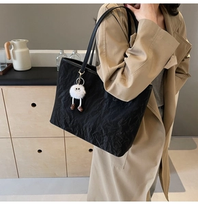 Detail of black pleated tote bag featuring a white plush charm and slim shoulder straps