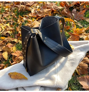 Détail du sac seau en cuir noir avec large bandoulière ornée d'œillets métalliques