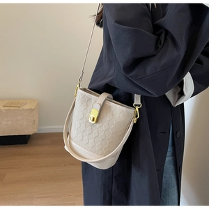 Détail d'un sac seau beige à texture tissée avec fermoir doré porté en bandoulière