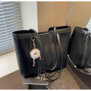 Detail of black matte leather tote bag with white contrast stitching and plush charm