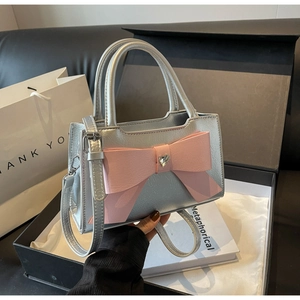 Silver square handbag with large pink bow and heart rhinestone on black leather sofa