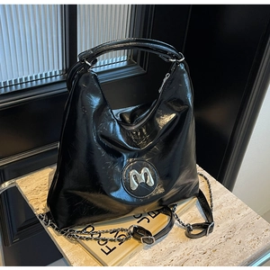 Detail of glossy black hobo bag with silver M logo and chain strap on marble surface