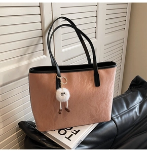 Detail of dusty pink tote bag with leather straps and cute plush pendant on fashion books