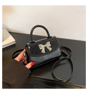 Detail of a mini black crossbody bag with cracked leather and silver metal bow
