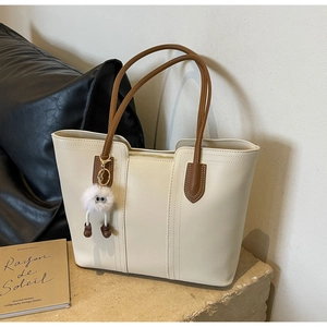 Detail of cream tote bag with brown handles and a cute fuzzy eye charm on a stone base