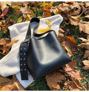 Détail du sac seau noir en cuir avec large bandoulière à œillets sur polaire blanche