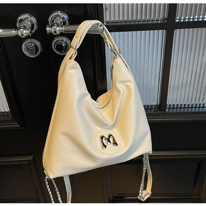 Detail of cream hobo bag with textured finish, metallic M emblem, and silver chain strap