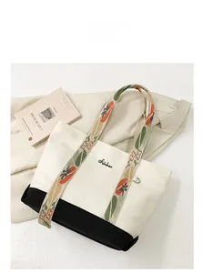 Détail du sac cabas en toile avec bandoulière fleurie et logo brodé sur le tissu