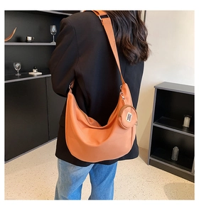 Détail du sac hobo orange avec une petite pochette ronde porté par un mannequin
