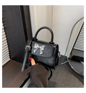 Detail of a black oil wax leather mini handbag with a silver metal bow accent