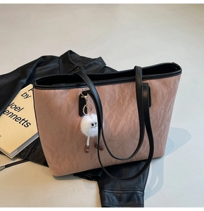 Detail of a pink tote bag with marble texture and a white plush charm on a black jacket